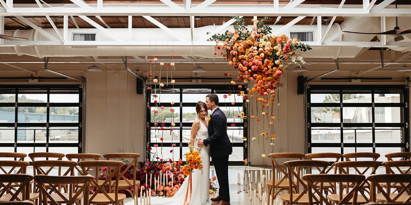 A bold ceremony setup at The Booking House in Manheim, PA, featuring suspended florals, colorful aisle arrangements and warm candlelight.