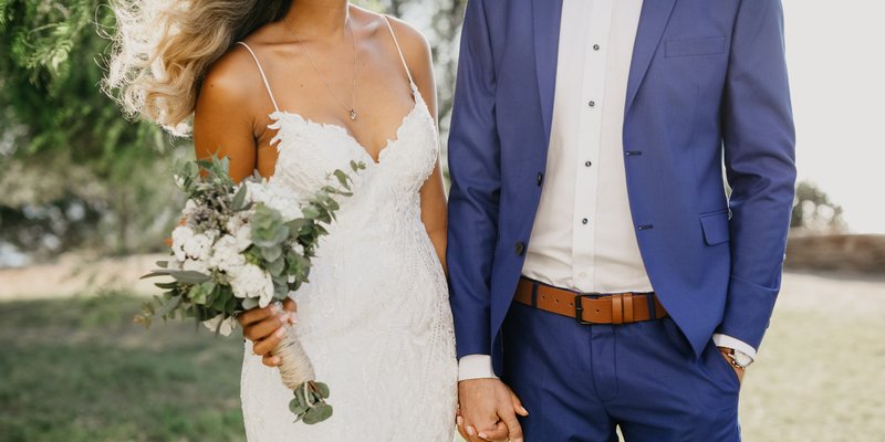 Bride holding white in green florals holding hands of groom in blue suit