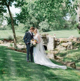 Bride and groom standing forehead to forehead on a luscious green, rolling hill