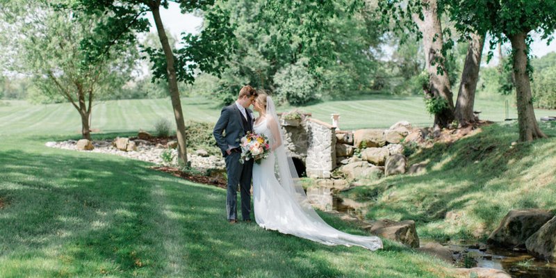 Bride and groom standing forehead to forehead on a luscious green, rolling hill